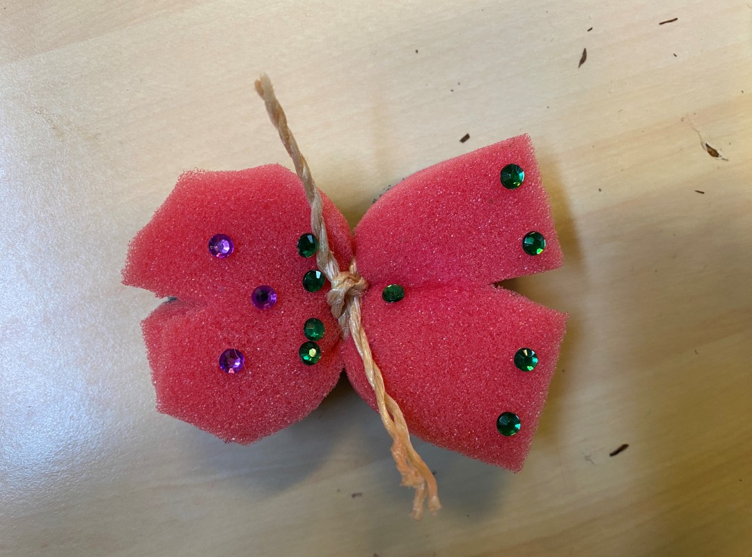 Een zelfgemaakte vlinder van een spons, glitters en een touwtje.