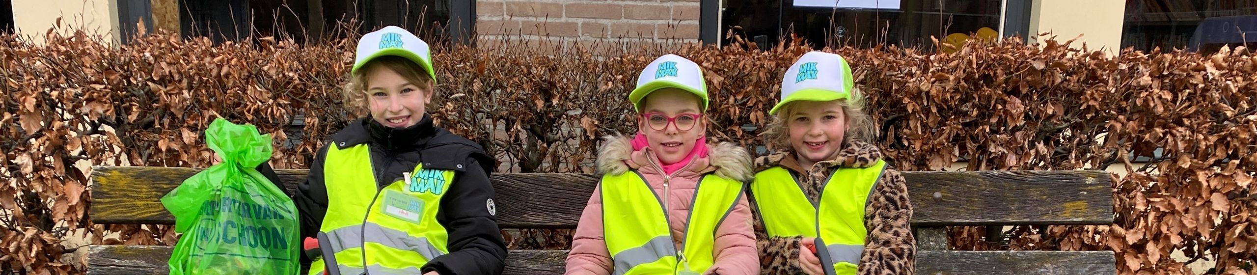 Drie vrolijke MikMakkers zitten op een bankje bij de bieb.